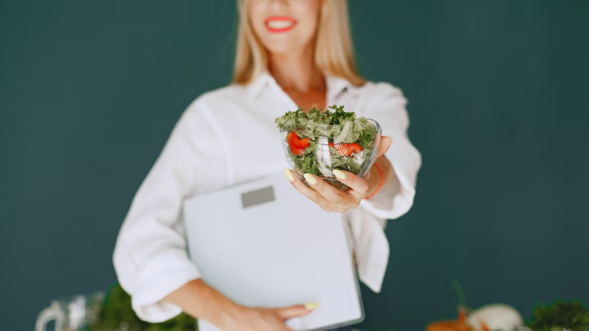 A woman with a vibrant smile offering a fresh salad bowl, promoting healthy eating.