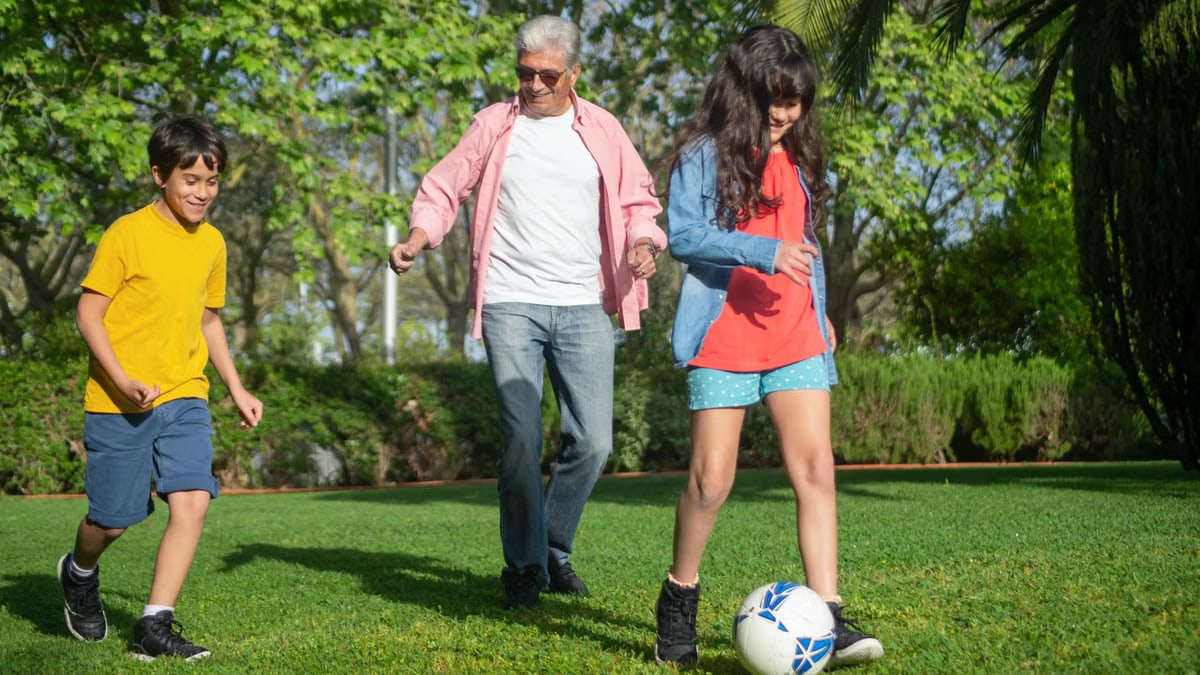 A joyful moment as a grandfather plays soccer with his grandchildren in a lush green park.